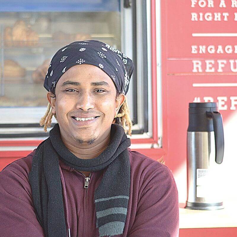 Man smiles outside of refugee coffee building
